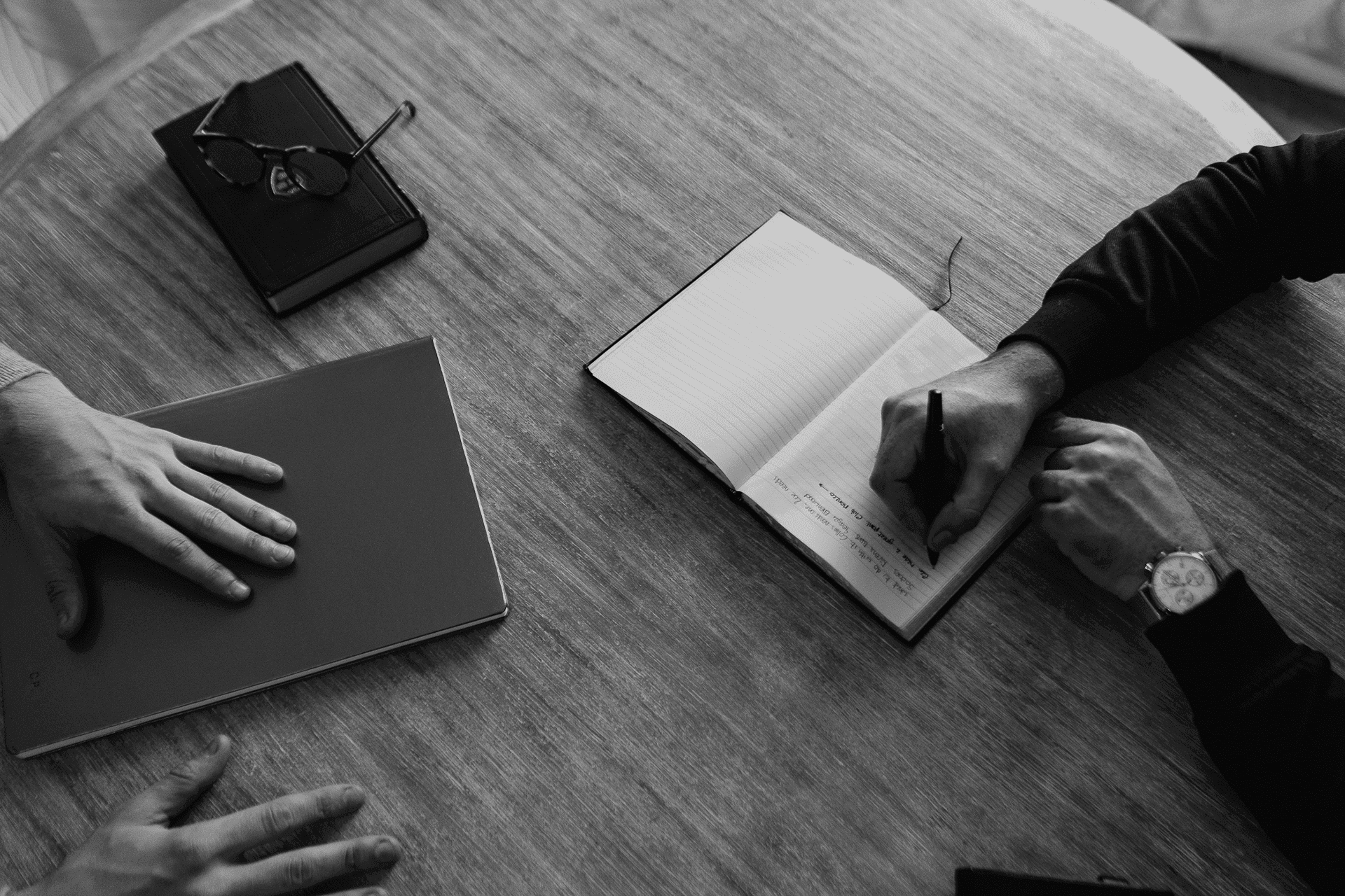 Hands writing in a notebook on a wooden table