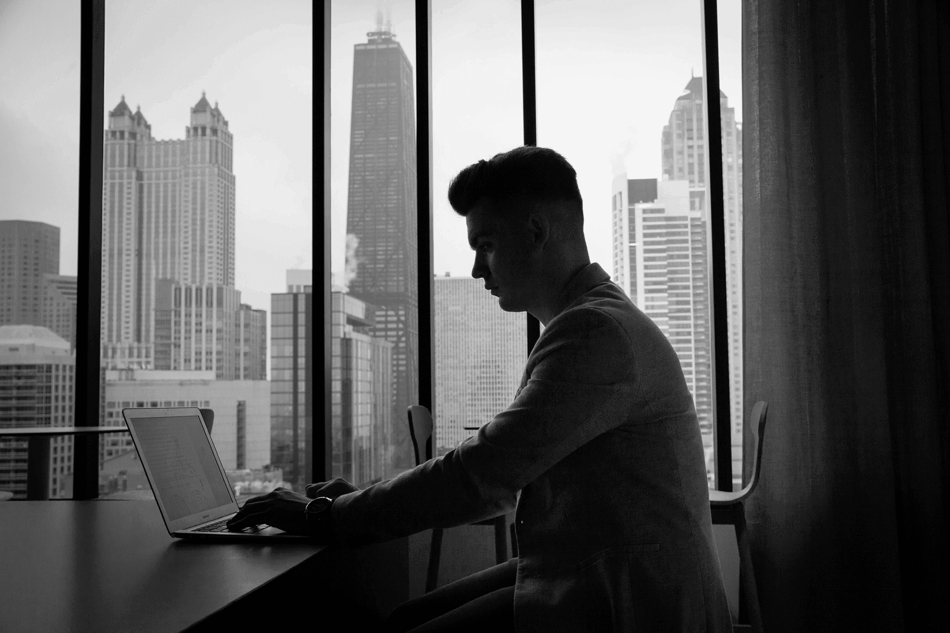 A man working on a laptop at a window above the Chicago skyline